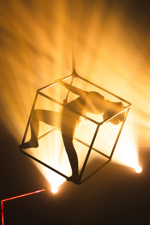 Acróbata aérea dentro de un cubo suspendido, a contraluz dorado